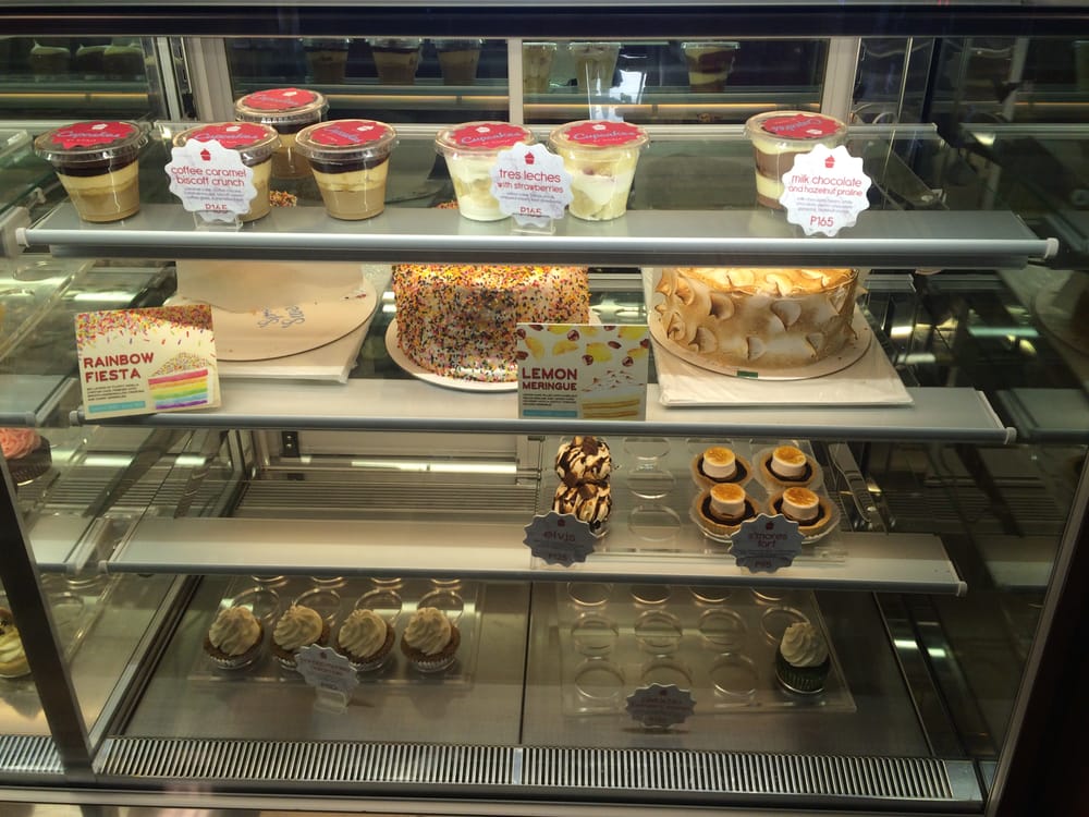 Display case with Rainbow Fiesta cake, Lemon Meringue, and cupcakes